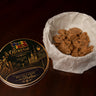 Creole-ish gold tin lid beside 20 Creole-ish Bites pecan praline bites packed in parchment paper